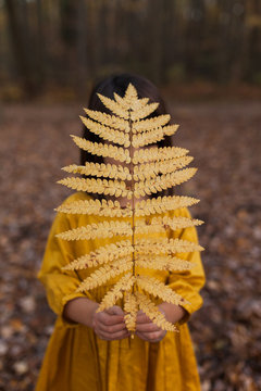 Girl hiding face behind a golden fern in autumn