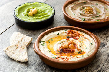 Different hummus bowls. Chickpea hummus, avocado hummus and lentils hummus on wooden table

