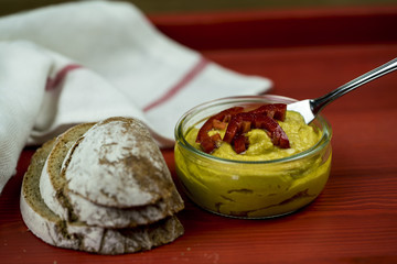 Beautiful, homemade curry hummus in a glass bowl with a red capsicum garnish and rustic rye bread