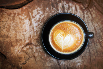 Cup of latte art coffee with heart shape on wooden texture