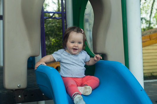 Happy little baby girl rolling down the hill on the playground