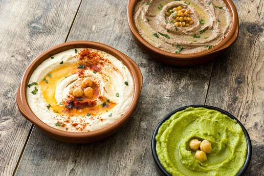 Different hummus bowls. Chickpea hummus, avocado hummus and lentils hummus on wooden table

