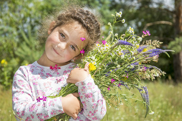 In summer there is a little sweet girl with a bouquet of wildflowers on the field.