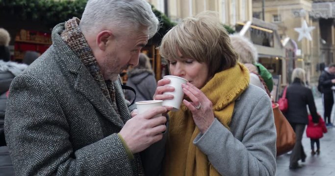Mature couple are enjoying a cup of coffee as they explore the town christmas market. 