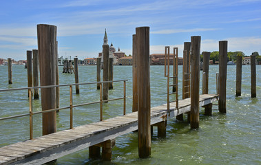 Obraz premium A mooring pier and mooring piles in the Dorsoduro quarter of Venice. The island of Giudecca can be seen across the Giudecca canal. Chiesa di San Georgio Maggiore stands out on the skyline. 