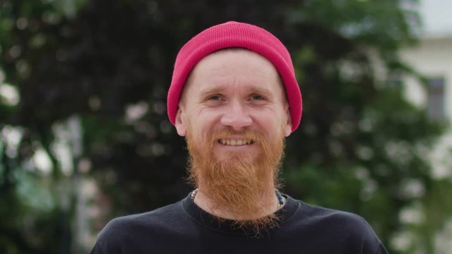 Young readhead hispter with beard and moustaches in jeans and T-shirt laughs suddenly. Outdoor. Cloudy. Medium. Stabilised. Portrait