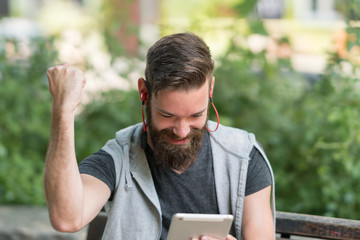 Fototapeta premium Exulting hipster guy with raised arm celebrating reading something on his digital tablet