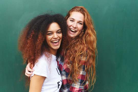 Portrait of two girlfriends laughing against of green background