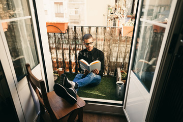 Latin man in the balcony sitting reading a book.