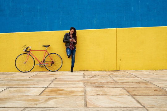 Young woman standing beside his bicycle using her smartphone