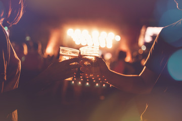 People with glasses toasting in front of silhouettes of concert crowd.