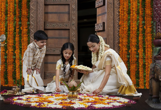 South Indian woman making a flower rangoli with son and daughter 