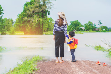 Mom holding hand of little son with backpack outdoors, back to school,looking back home with floods.