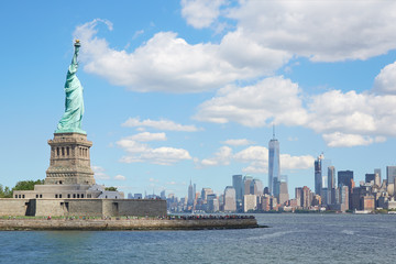 Statue of Liberty island and New York city skyline in a sunny day, white clouds
