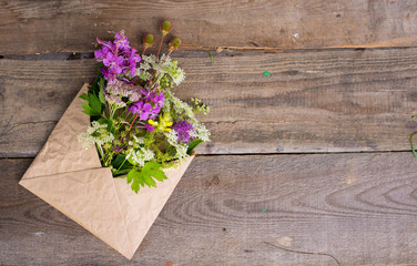 Wild field flowers in craft paper envelope over wooden background
