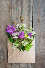 Fototapeta na wymiar Wild field flowers in craft paper envelope over wooden background