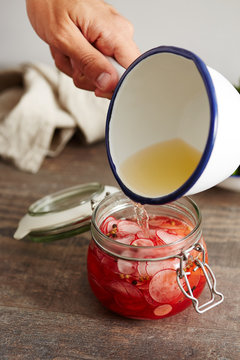 Close-up of man's hand pouring pickle in jar with spiced radish