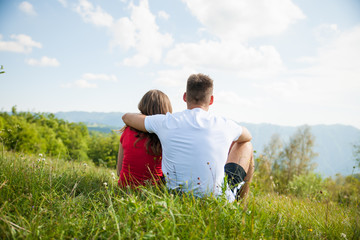 active couple rests on a mountain peak looking on a mountain landscape
