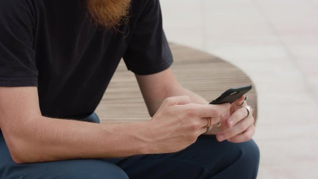 Young readhead hispter with beard and moustaches in jeans and T-shirt hold smartfone. Outdoor. Cloudy. Medium. Stabilised. Portrait
