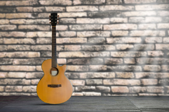 acoustic guitar on the wooden floor against brick wall background. © thithawat