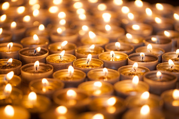 Burning bright. Golden warm glow from candle flames. Many beautiful lit tealight candles glowing. - obrazy, fototapety, plakaty