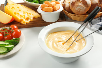 Cheese fondue in plate with different products on white table
