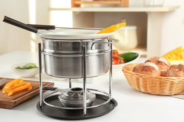 Stick with piece of bell pepper and cheese fondue in pot on table