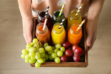 Young woman holding wooden crate with delicious juices in bottles