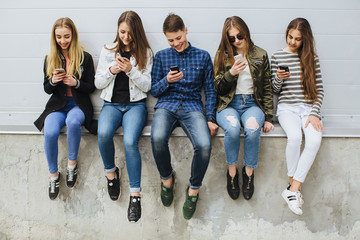 Group of teenagers sitting outdoors using their mobile phones.