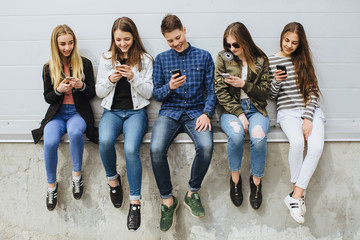 Group of teenagers sitting outdoors using their mobile phones.