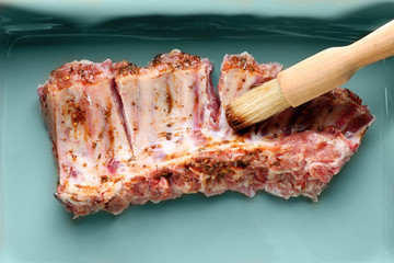 Baking tray with raw pork ribs and basting brush, closeup