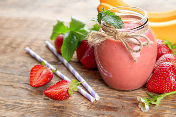 Jar of delicious strawberry homemade smoothie on wooden background