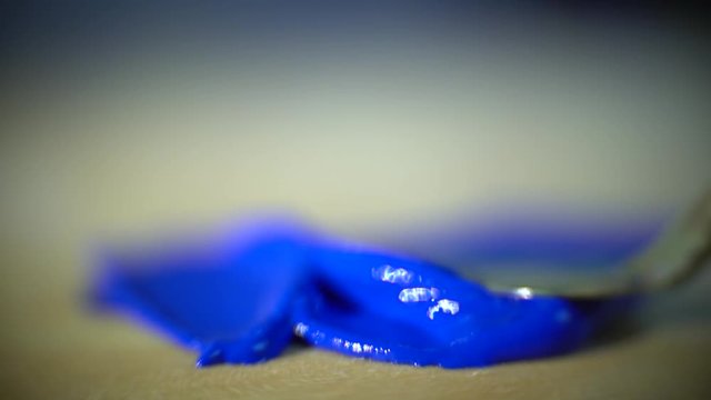 Macro shooting as metal putty knife smears the blue paint on a wooden palette