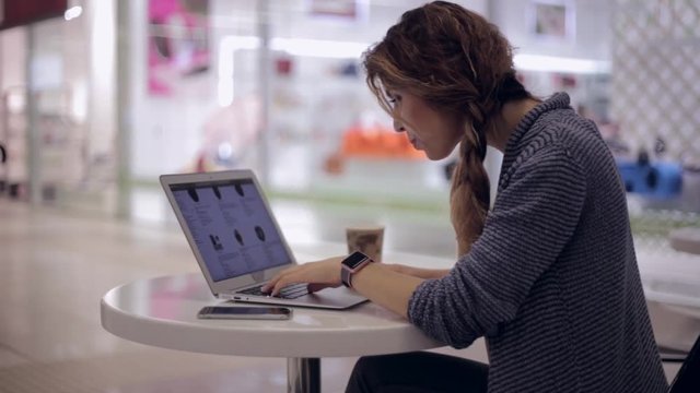 An attractive woman is looking in the online store for a new electronic device using a laptop