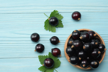 black currant in wooden bowl with green leaf on blue wooden background. top view with copy space