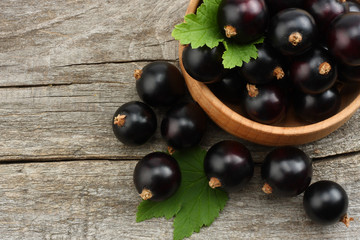 black currant in wooden bowl with green leaf on old wooden background. top view