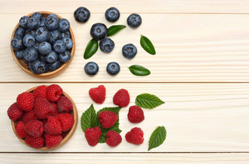 mix of blueberries, raspberries in wooden bowl on light wooden table background. top view with copy space