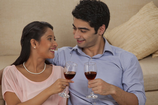 Smiling young couple holding wineglass while looking at each other 