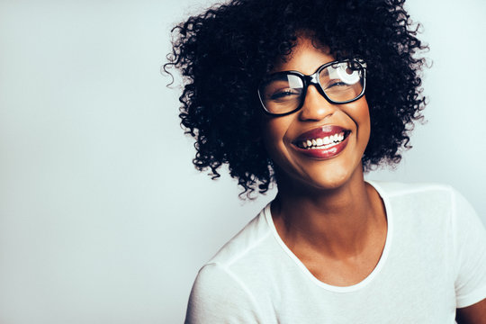 Laughing young African woman wearing glasses against a gray back