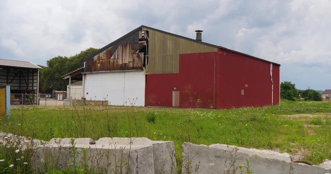 A daytime exterior (DX) establishing shot of an old abandoned factory or warehouse in a small New England town.  	