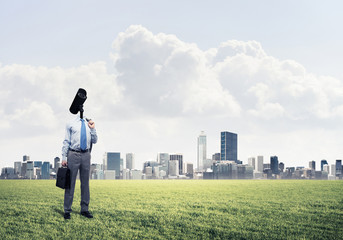Camera headed man standing on green grass against modern citysca