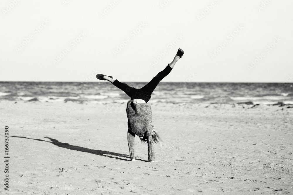 Wall mural black and white portrait of funny white caucasian child kid teenager doing cartwheel playing on beac