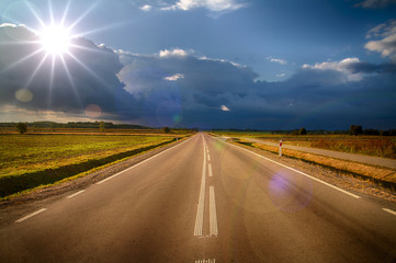 Asphalt road running towards the horizon illuminated from the front of the sun