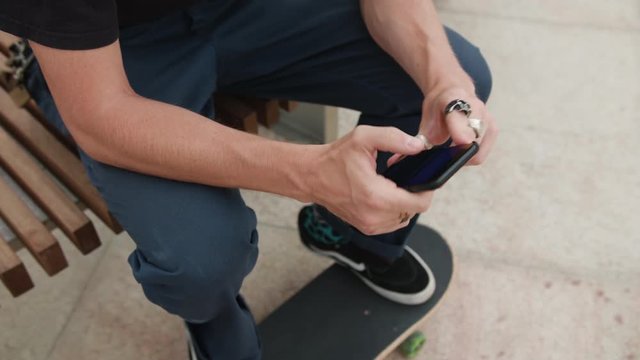 Young readhead hispter with beard and moustaches in jeans and T-shirt writes a message on smartfone. Outdoor. Cloudy. Medium. Stabilised. Portrait. From above