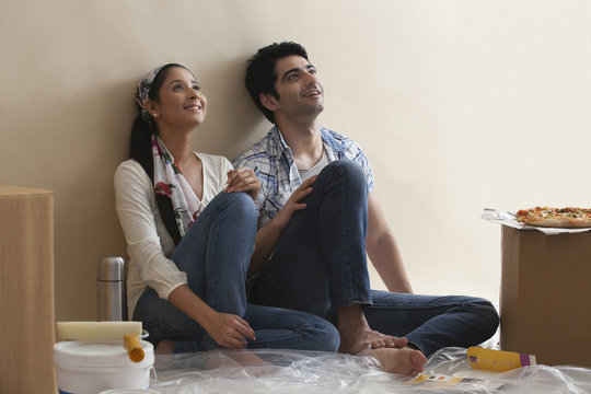 Smiling young couple leaning against the wall while thinking 