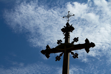 Old, historic wooden cross against the sky with white clouds