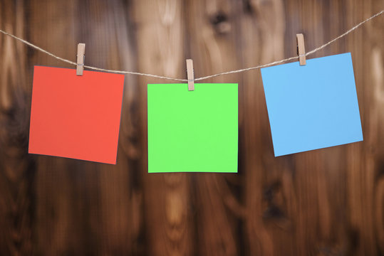 Close up of three red yellow and blue note papers hung by wooden clothes pegs on a brown wooden background