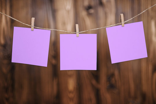 Close up of three violet note papers hung by wooden clothes pegs on a brown wooden background