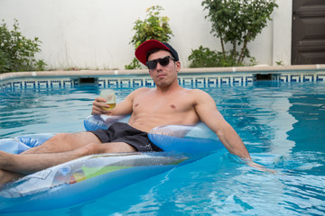 Young strong man drinking beer on an air bed in the pool. 