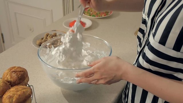 Closeup Young woman in the kitchen whipping with a white cream mixer in a transparent dish